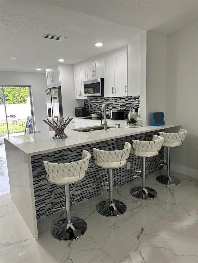 kitchen featuring a kitchen bar, sink, white cabinets, and appliances with stainless steel finishes