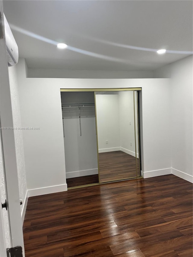 unfurnished bedroom with a closet, a wall mounted air conditioner, and dark hardwood / wood-style floors