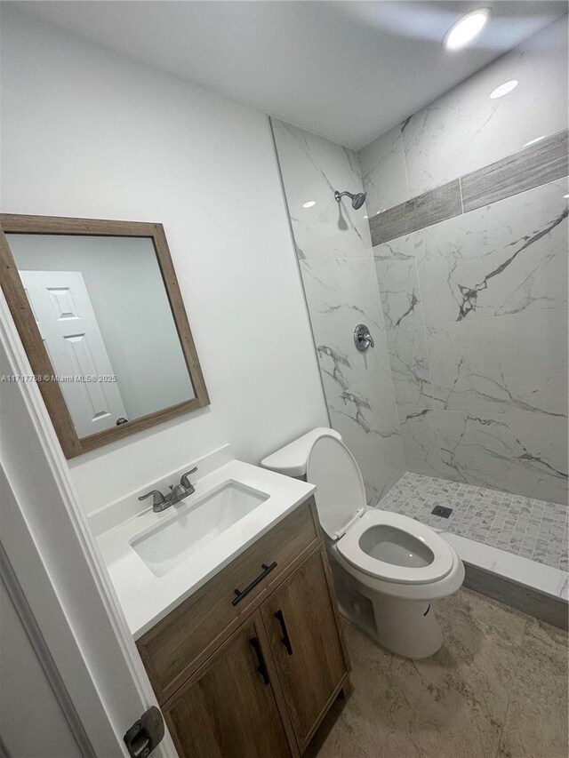 bathroom with tiled shower, vanity, and toilet