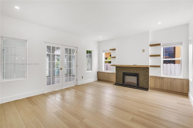 unfurnished living room with light wood-type flooring, a tile fireplace, and french doors