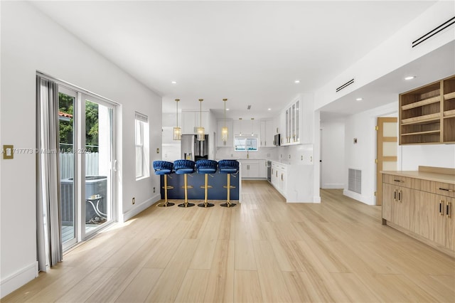 kitchen featuring decorative light fixtures, light hardwood / wood-style floors, white cabinetry, a breakfast bar area, and stainless steel appliances