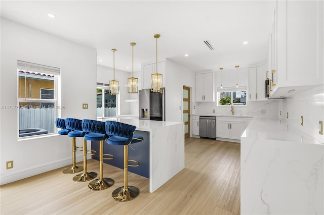 kitchen featuring a kitchen bar, light stone counters, stainless steel appliances, pendant lighting, and white cabinets