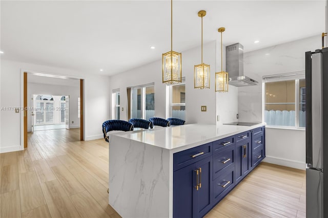 kitchen with blue cabinets, hanging light fixtures, wall chimney exhaust hood, kitchen peninsula, and stainless steel refrigerator