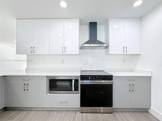 kitchen featuring wall chimney exhaust hood, white cabinetry, and appliances with stainless steel finishes