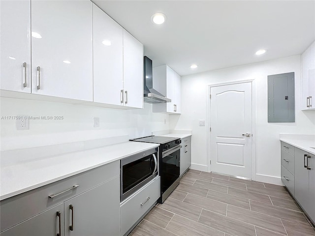 kitchen featuring appliances with stainless steel finishes, gray cabinetry, wall chimney range hood, electric panel, and white cabinetry