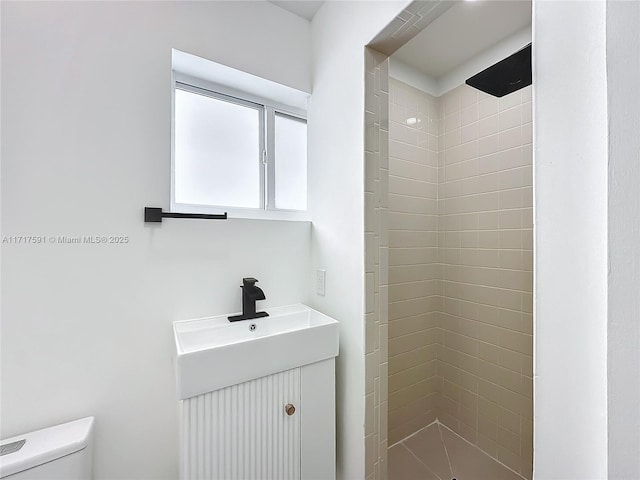 bathroom featuring a tile shower, vanity, and toilet