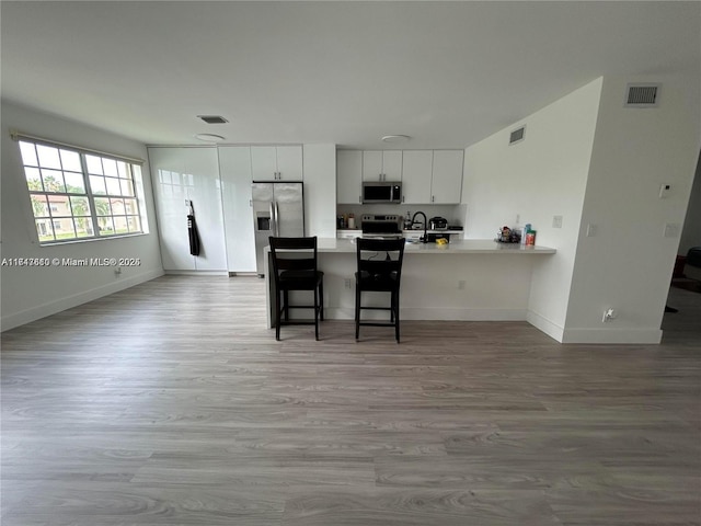 kitchen featuring white cabinetry, stainless steel appliances, kitchen peninsula, light hardwood / wood-style floors, and a kitchen bar