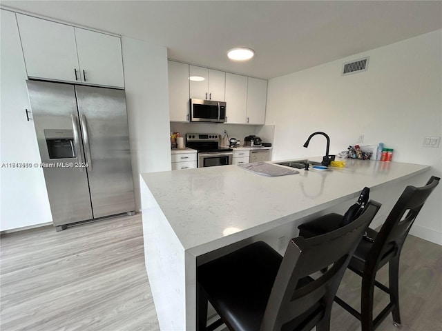 kitchen with kitchen peninsula, appliances with stainless steel finishes, sink, white cabinetry, and a breakfast bar area