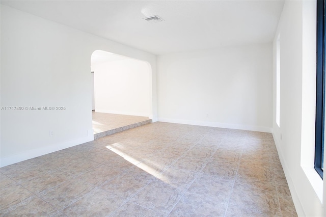 empty room with visible vents, tile patterned floors, and arched walkways