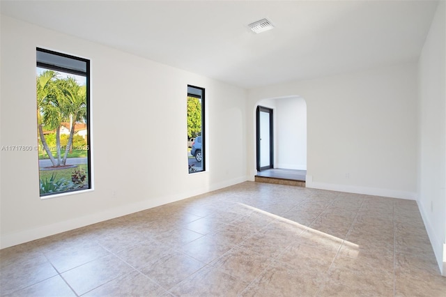tiled empty room with arched walkways, visible vents, baseboards, and a healthy amount of sunlight