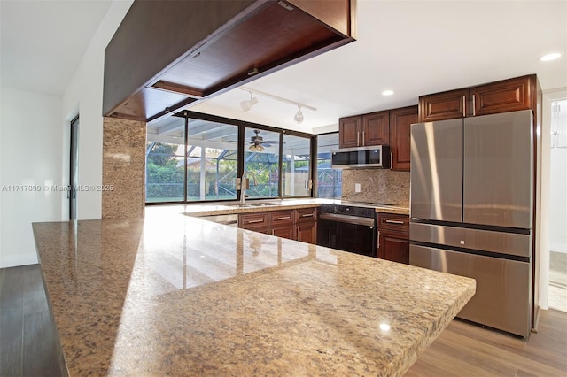 kitchen with sink, light hardwood / wood-style flooring, stainless steel appliances, light stone countertops, and kitchen peninsula