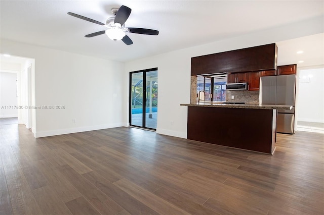 unfurnished living room with dark wood-style flooring, baseboards, and a ceiling fan