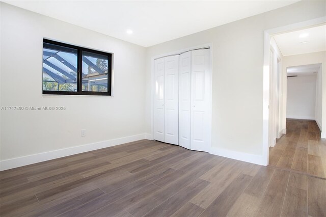 unfurnished bedroom with a closet, baseboards, recessed lighting, and wood finished floors