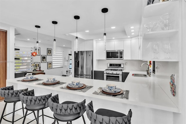 kitchen with kitchen peninsula, appliances with stainless steel finishes, sink, white cabinetry, and a breakfast bar area