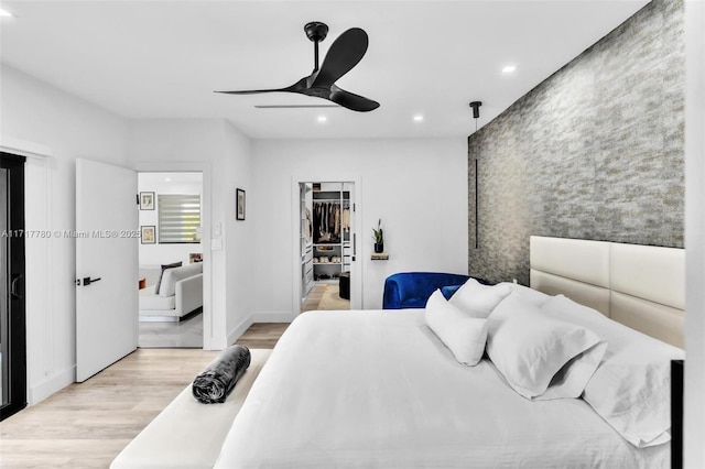 bedroom featuring a closet, a walk in closet, light hardwood / wood-style floors, and ceiling fan