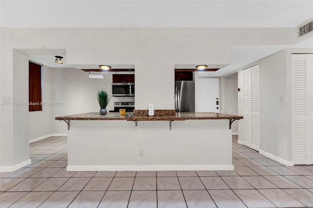 kitchen featuring a kitchen bar, kitchen peninsula, light tile patterned floors, and appliances with stainless steel finishes