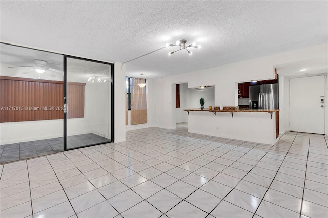 unfurnished living room with ceiling fan, light tile patterned flooring, and a textured ceiling