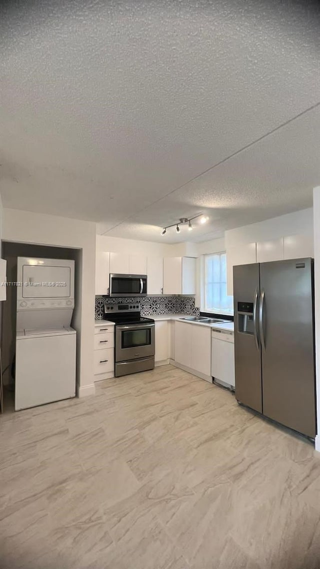 kitchen featuring stacked washer and dryer, a textured ceiling, track lighting, white cabinets, and appliances with stainless steel finishes