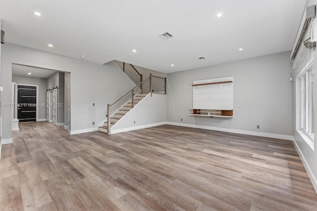 unfurnished living room with a barn door and light hardwood / wood-style flooring