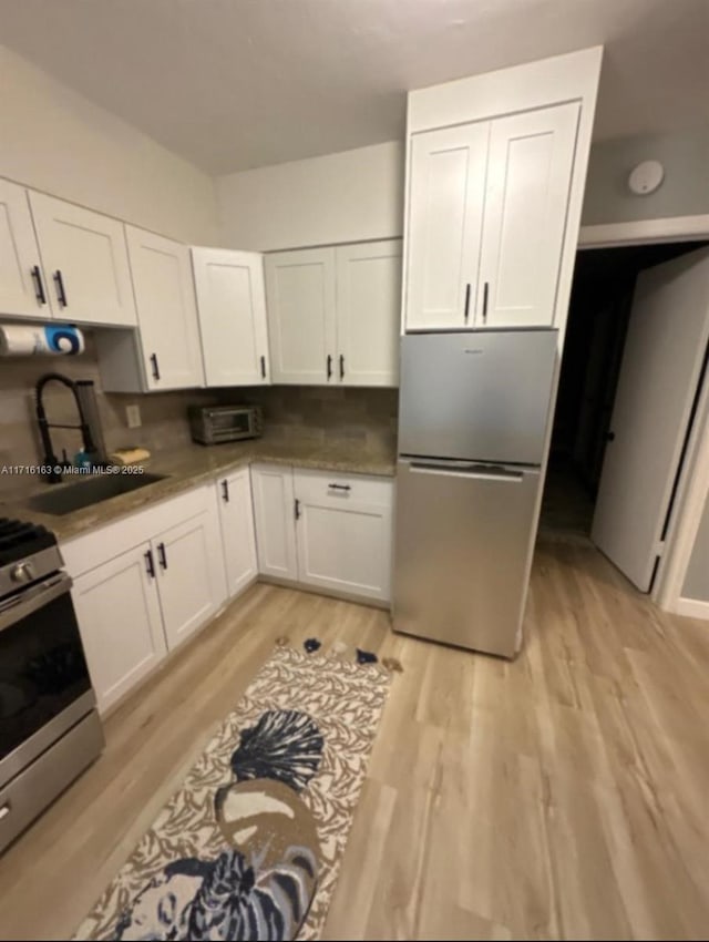 kitchen featuring backsplash, stainless steel appliances, sink, light hardwood / wood-style floors, and white cabinetry