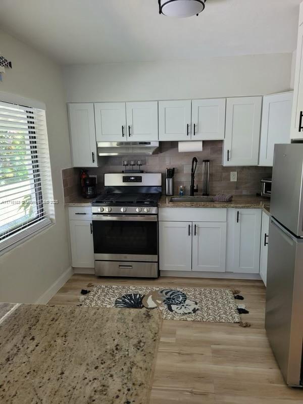 kitchen featuring sink, decorative backsplash, light wood-type flooring, white cabinetry, and stainless steel appliances