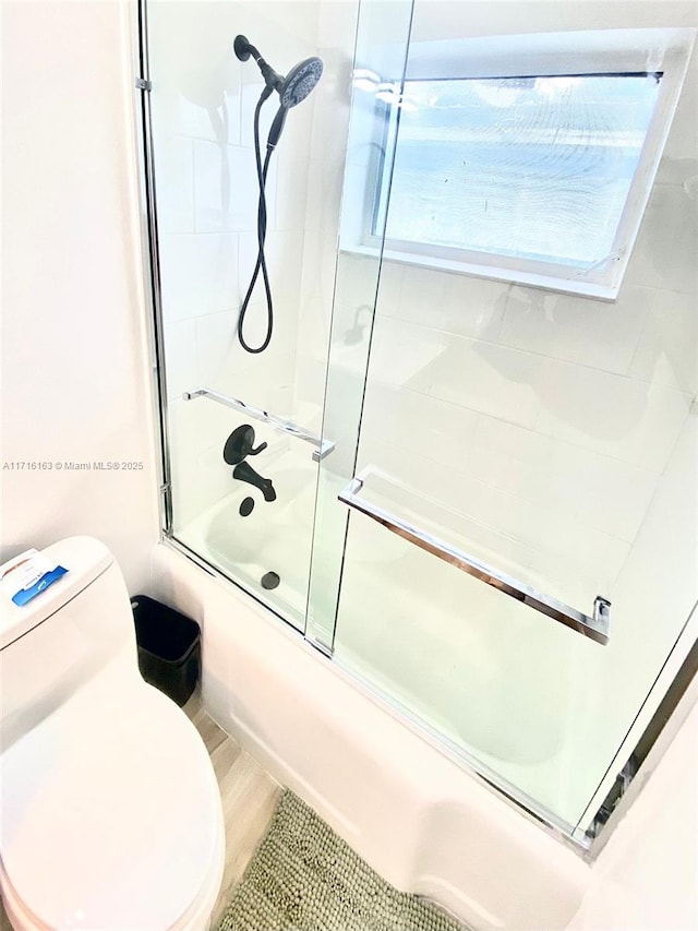 bathroom featuring toilet and combined bath / shower with glass door