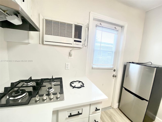 kitchen featuring light wood-type flooring, gas stovetop, a wall mounted AC, white cabinetry, and stainless steel refrigerator