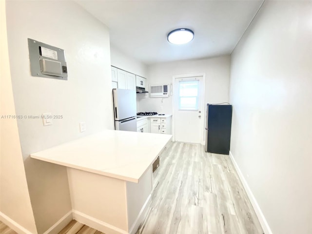 kitchen featuring kitchen peninsula, light wood-type flooring, an AC wall unit, white fridge, and white cabinetry