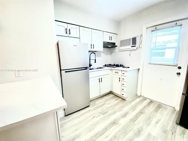 kitchen with white gas cooktop, a wall unit AC, sink, white cabinetry, and stainless steel refrigerator