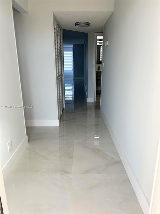 corridor featuring a textured ceiling, marble finish floor, and baseboards