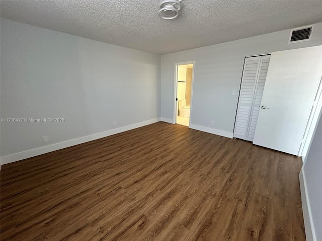 unfurnished bedroom featuring a textured ceiling, dark wood-type flooring, visible vents, baseboards, and a closet