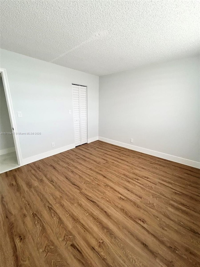 unfurnished room featuring dark wood-style floors, a textured ceiling, and baseboards