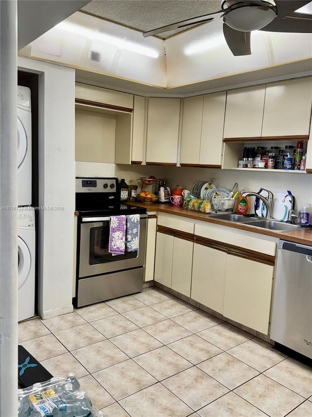 kitchen featuring stacked washing maching and dryer, sink, stainless steel appliances, and cream cabinetry