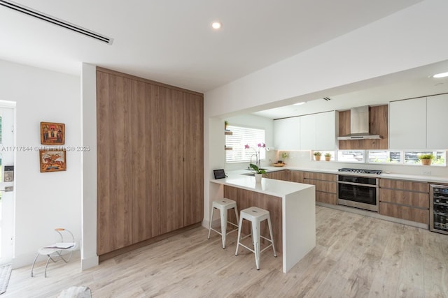 kitchen with wall chimney exhaust hood, stainless steel appliances, kitchen peninsula, a breakfast bar area, and white cabinets