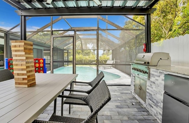 view of patio featuring glass enclosure, area for grilling, and exterior kitchen