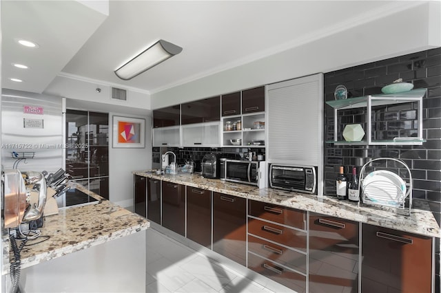 kitchen featuring decorative backsplash, dark brown cabinets, light stone counters, and ornamental molding