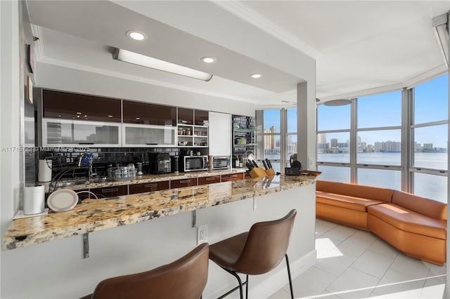 kitchen with a water view, ornamental molding, tasteful backsplash, light tile patterned flooring, and light stone counters