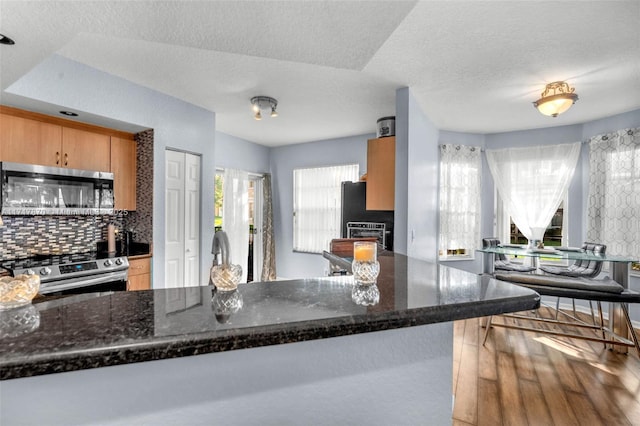 kitchen featuring backsplash, kitchen peninsula, dark stone countertops, a textured ceiling, and appliances with stainless steel finishes