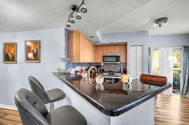 kitchen featuring kitchen peninsula, decorative backsplash, light hardwood / wood-style floors, and appliances with stainless steel finishes