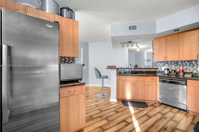 kitchen with sink, stainless steel appliances, a textured ceiling, and light hardwood / wood-style floors