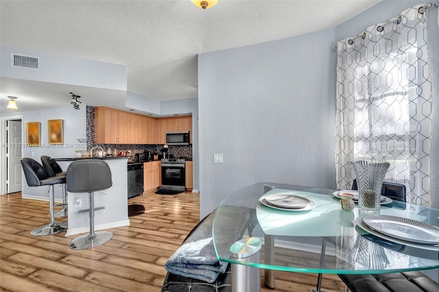 kitchen with sink, light wood-type flooring, a textured ceiling, appliances with stainless steel finishes, and tasteful backsplash