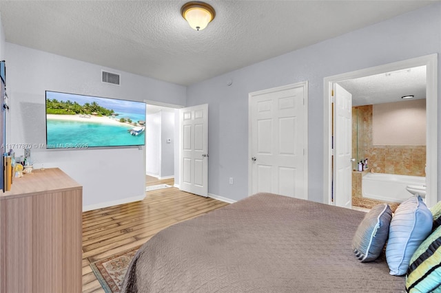 bedroom featuring connected bathroom, light hardwood / wood-style floors, and a textured ceiling