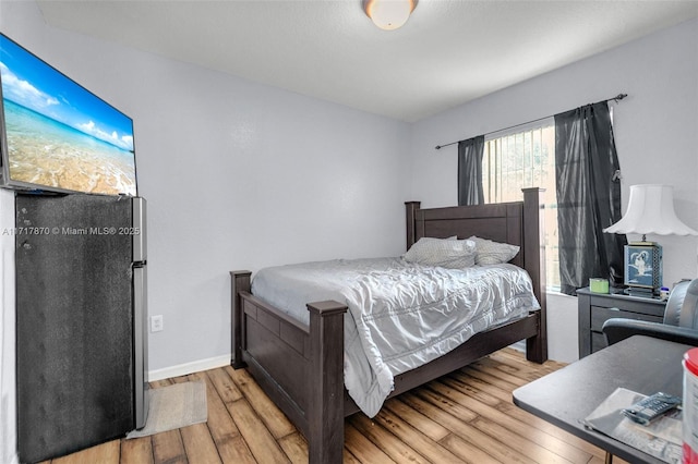 bedroom with stainless steel fridge and light hardwood / wood-style floors