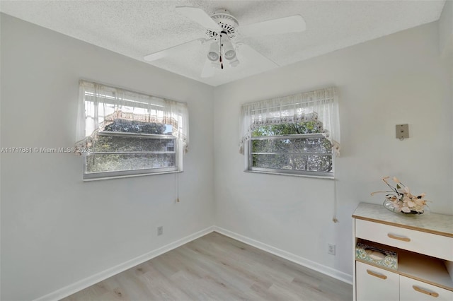 unfurnished room with ceiling fan, light wood-type flooring, and a textured ceiling