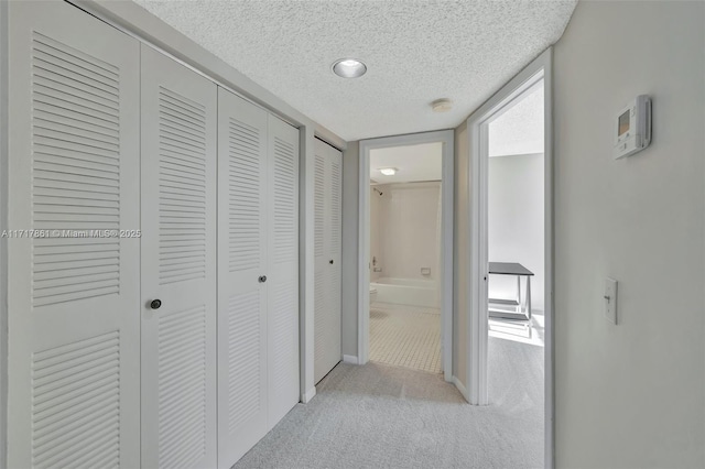 hall with light colored carpet and a textured ceiling