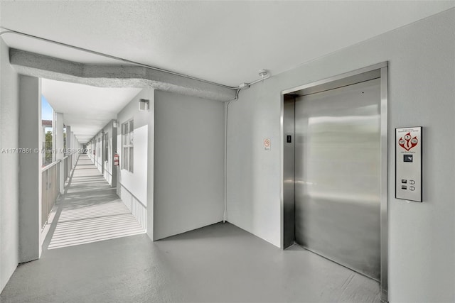 hall with concrete flooring, a textured ceiling, and elevator