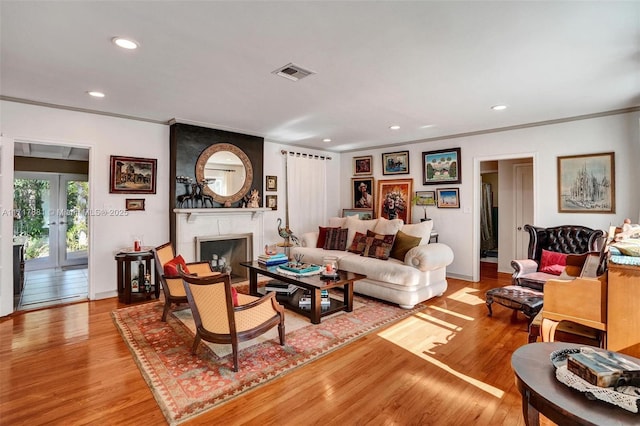 living room with crown molding, a fireplace, french doors, and light wood-type flooring