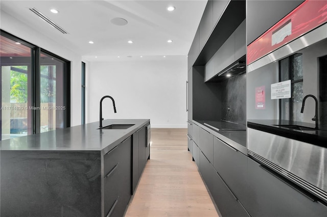 kitchen with tasteful backsplash, sink, a spacious island, and light hardwood / wood-style floors