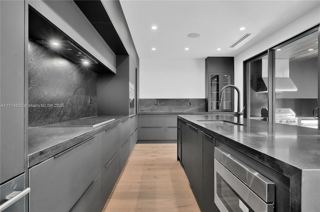 kitchen featuring stainless steel microwave, backsplash, sink, light wood-type flooring, and stainless steel counters