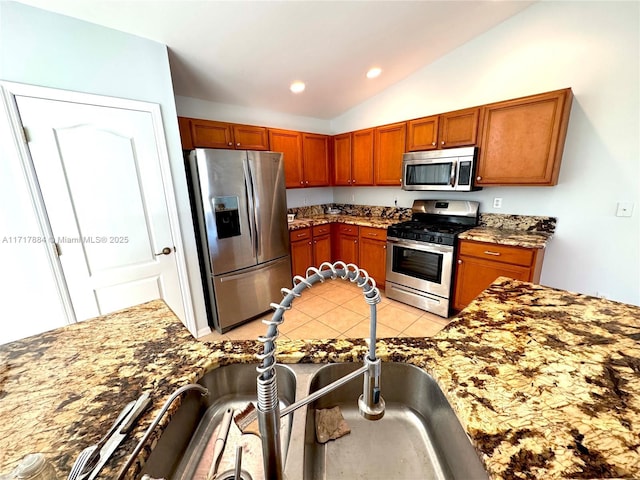 kitchen featuring sink, stone countertops, lofted ceiling, light tile patterned floors, and appliances with stainless steel finishes